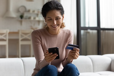 woman smiling while holding a cellphone and a credit card