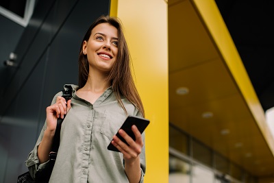woman with a backpack smiling and holding a cellphone