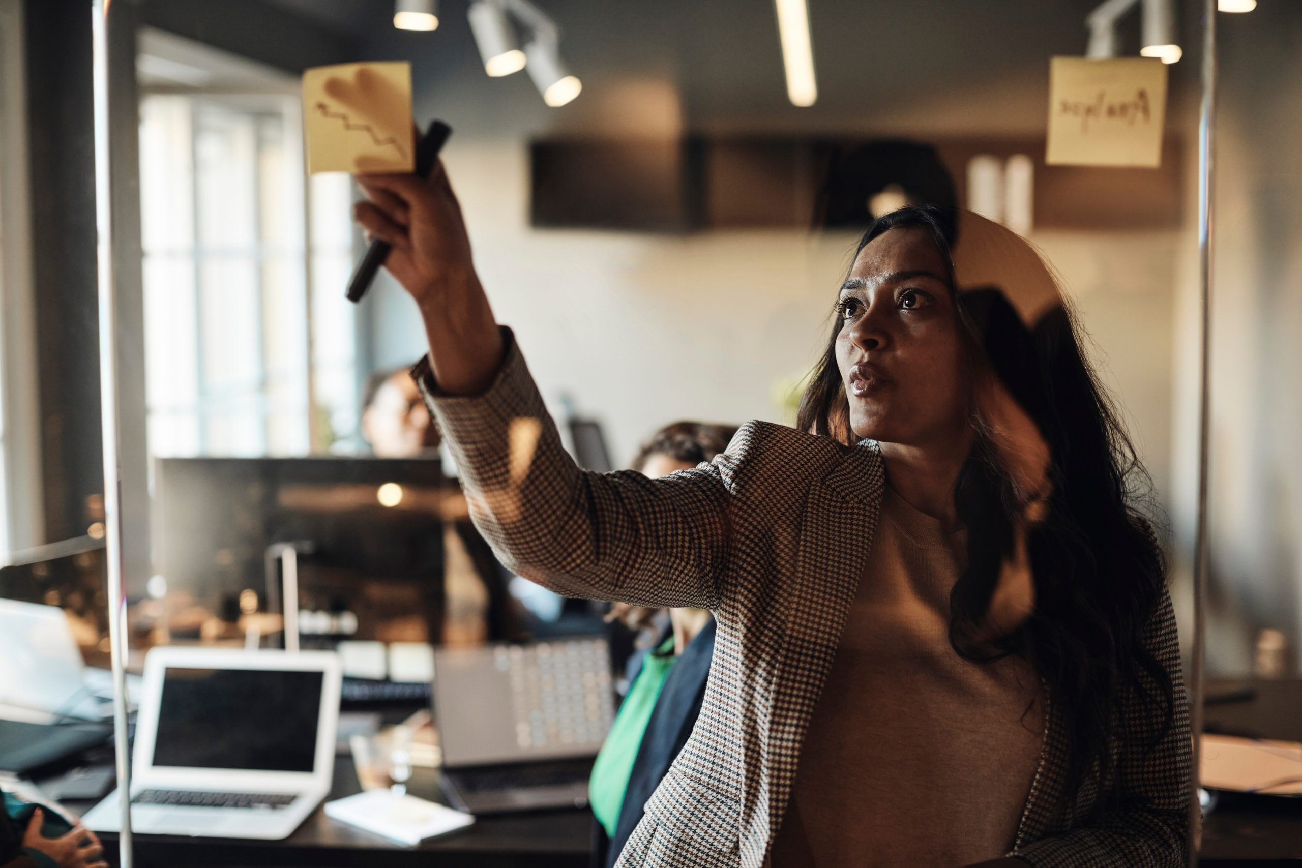 Mature Business woman Sticking Adhesive Note On Glass Wall In Office